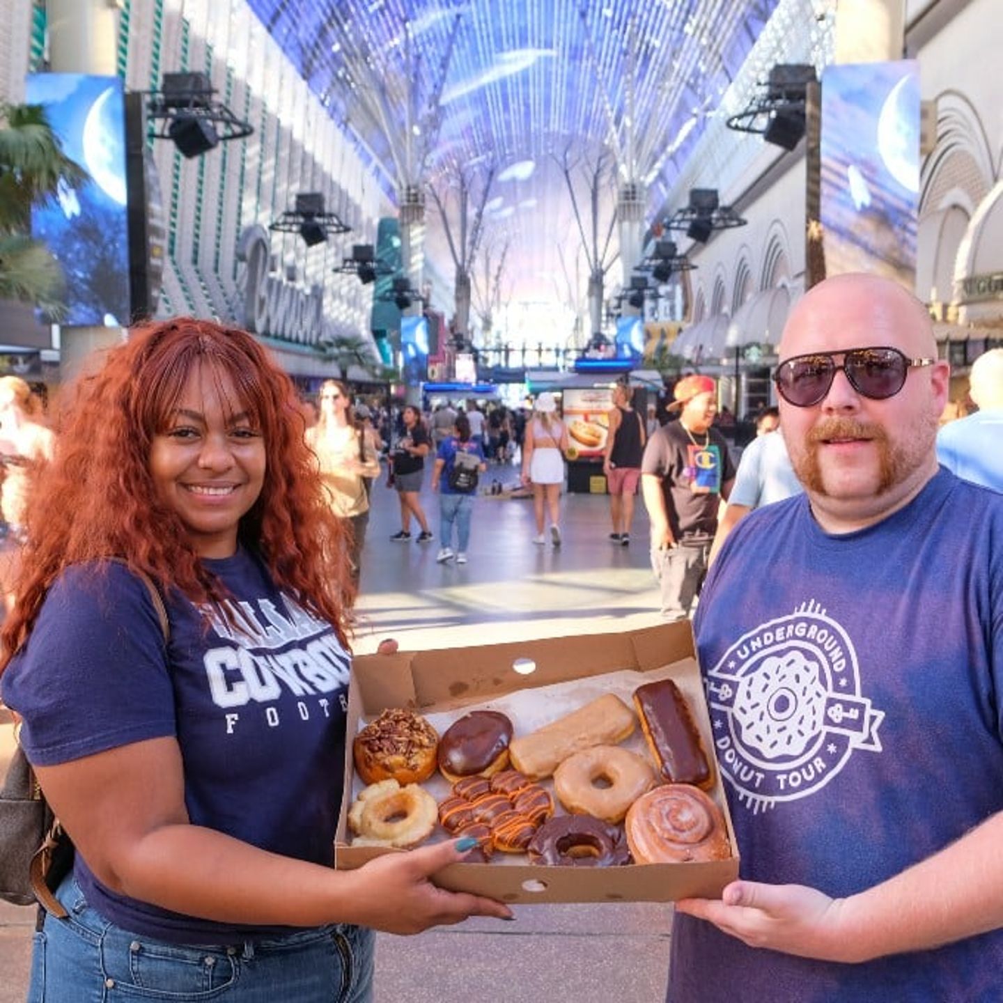 Two people holding box of donuts